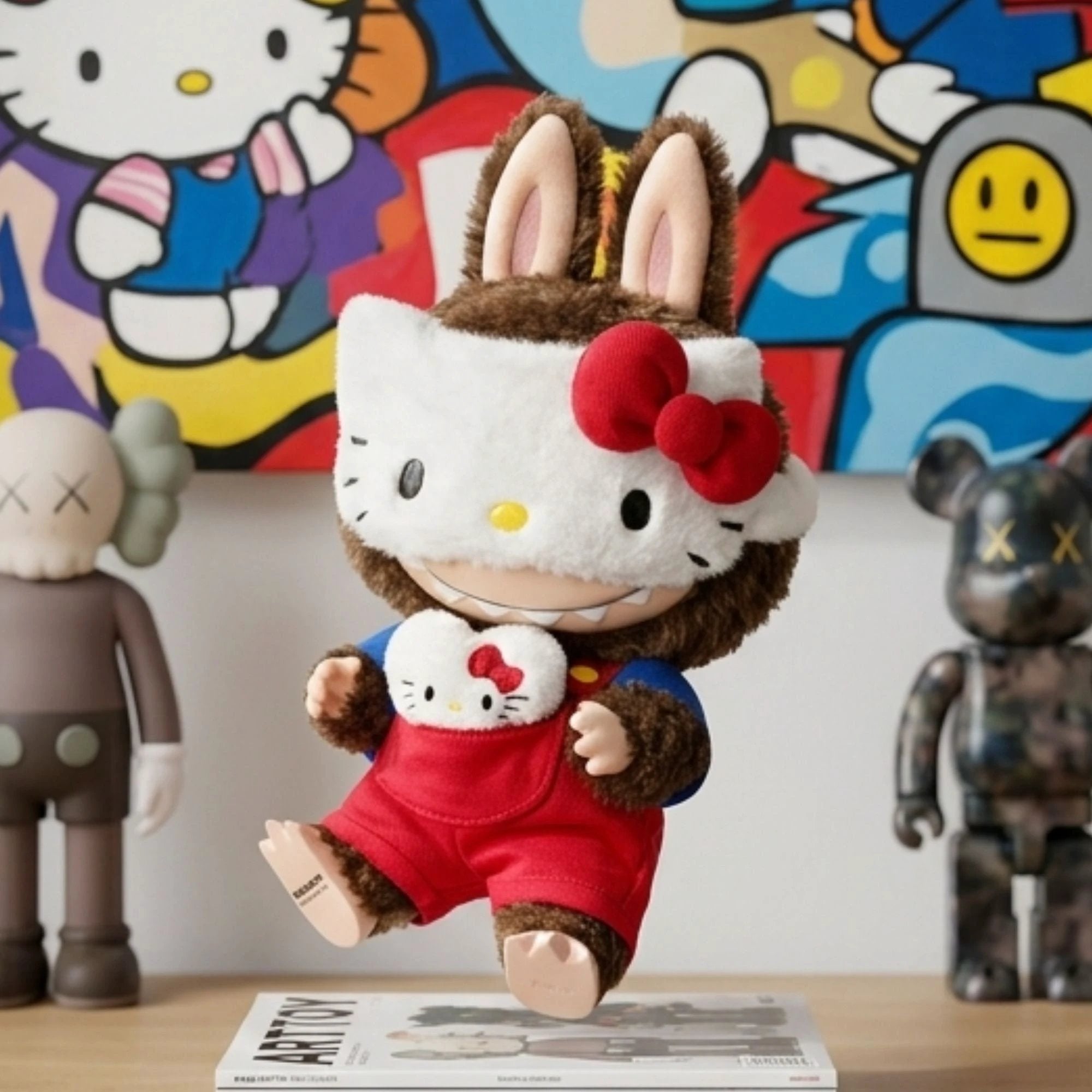 Figurine d'art en peluche Labubu portant le costume Hello Kitty, exposée sur une étagère de collection avec des livres et des sculptures d'artistes urbains.